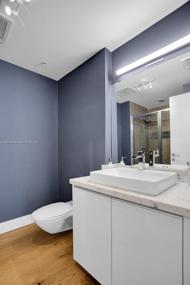 bathroom featuring wood-type flooring, toilet, vanity, and a shower with shower door