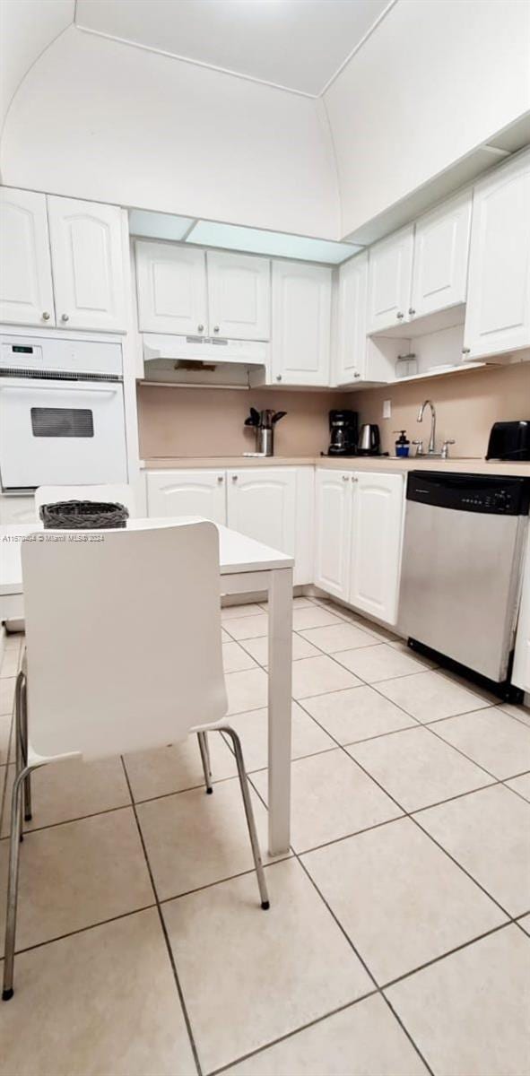 kitchen with light tile patterned floors, oven, white cabinetry, and stainless steel dishwasher