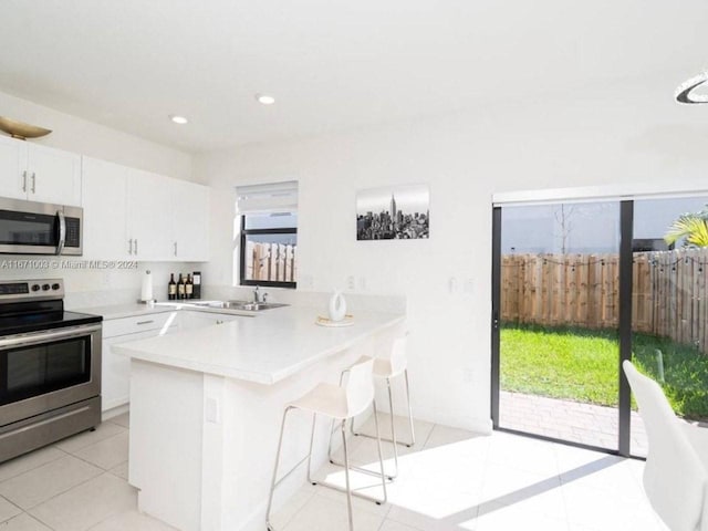 kitchen featuring appliances with stainless steel finishes, a breakfast bar, white cabinets, kitchen peninsula, and sink