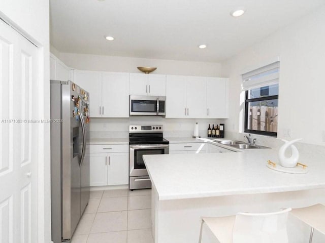 kitchen with light tile patterned flooring, sink, white cabinets, kitchen peninsula, and appliances with stainless steel finishes