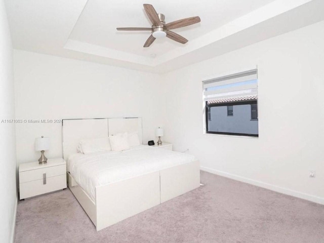 unfurnished bedroom with a tray ceiling, light carpet, and ceiling fan