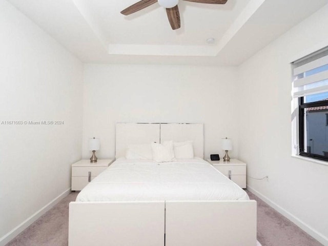 carpeted bedroom featuring a tray ceiling and ceiling fan