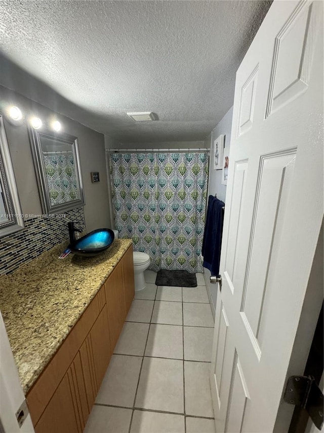 bathroom featuring tile patterned flooring, a textured ceiling, toilet, vanity, and curtained shower