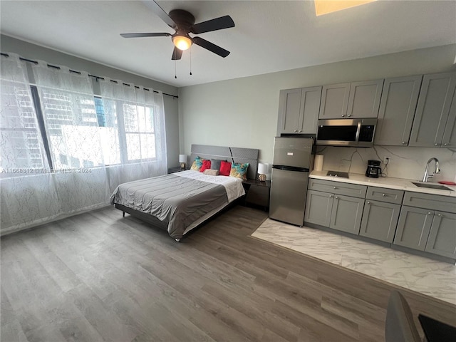 bedroom with light hardwood / wood-style flooring, ceiling fan, sink, and stainless steel refrigerator