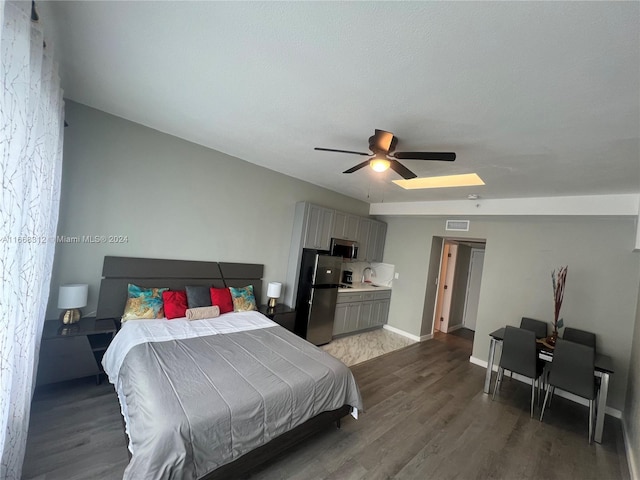 bedroom featuring dark hardwood / wood-style flooring, ceiling fan, lofted ceiling with skylight, and stainless steel fridge