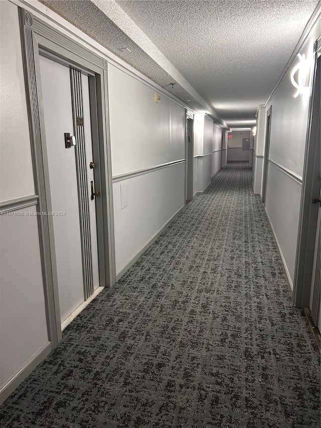 corridor featuring a textured ceiling and dark carpet