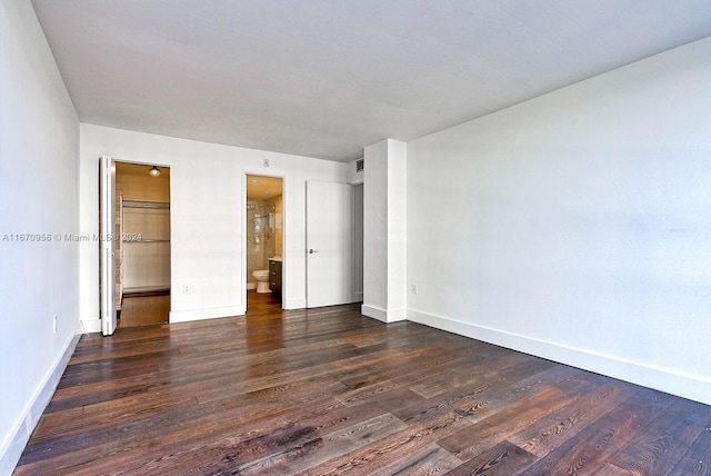 unfurnished bedroom with a spacious closet, dark wood-type flooring, ensuite bathroom, and a closet