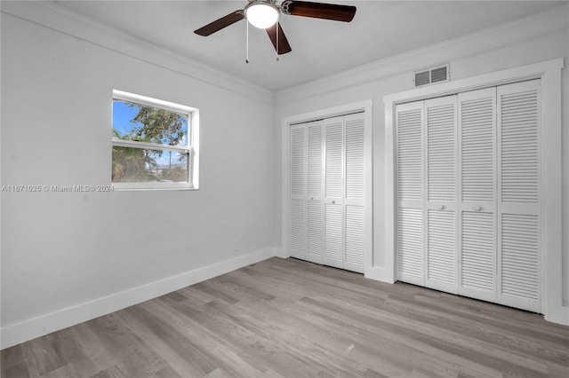 unfurnished bedroom with ceiling fan, light wood-type flooring, two closets, and ornamental molding