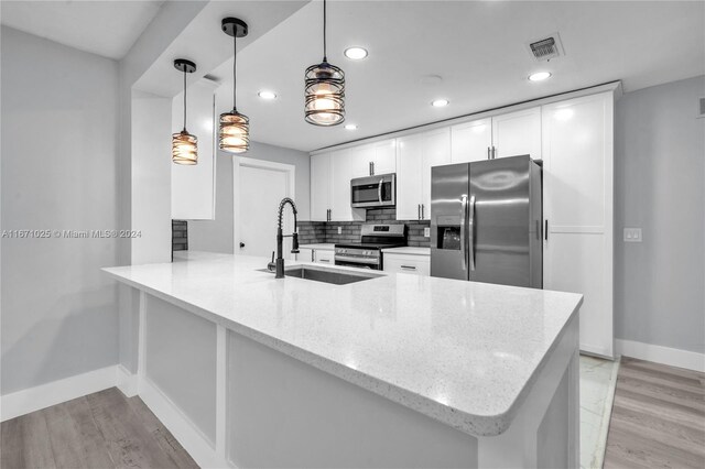 kitchen featuring appliances with stainless steel finishes, white cabinetry, kitchen peninsula, pendant lighting, and light wood-type flooring