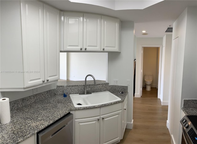 kitchen with sink, stone counters, white cabinetry, hardwood / wood-style flooring, and stainless steel appliances