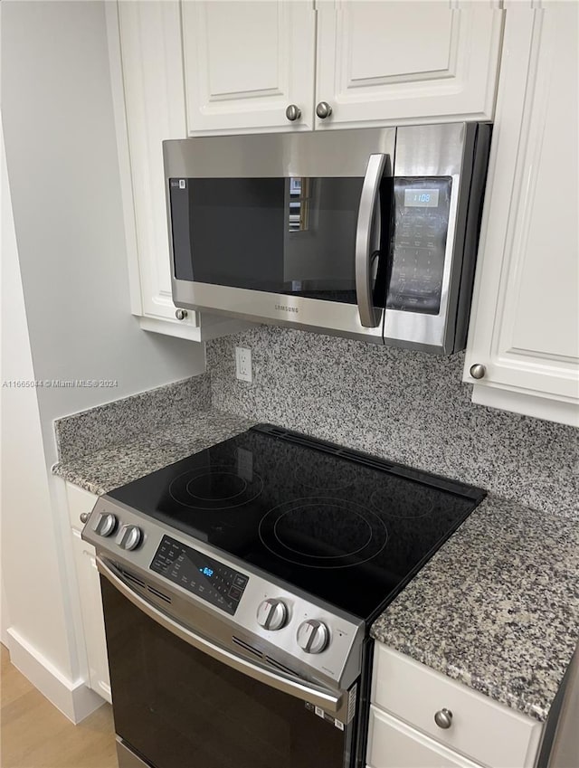 kitchen with stone counters, white cabinetry, stainless steel appliances, light wood-type flooring, and decorative backsplash