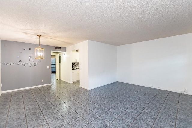 empty room featuring a textured ceiling and a chandelier