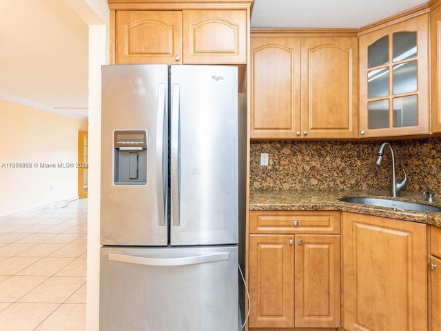 kitchen featuring dark stone counters, tasteful backsplash, sink, stainless steel refrigerator with ice dispenser, and light tile patterned floors