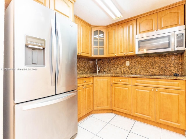 kitchen with dark stone counters, tasteful backsplash, light tile patterned flooring, sink, and appliances with stainless steel finishes