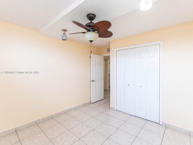 unfurnished bedroom with ceiling fan, a textured ceiling, a closet, and light tile patterned floors