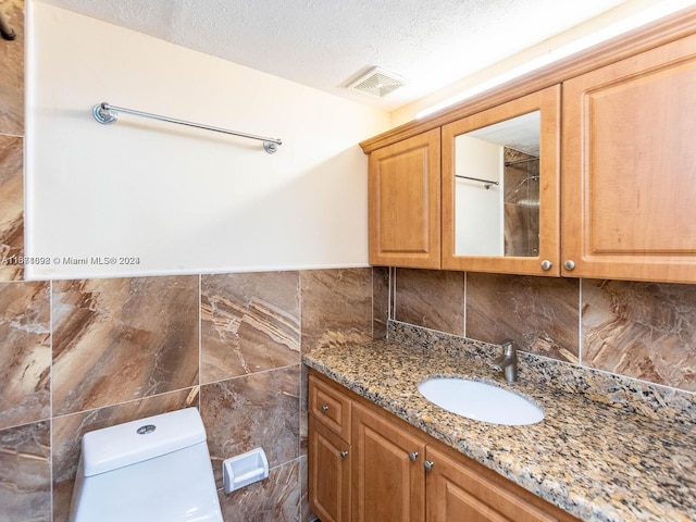 bathroom featuring tile walls, a textured ceiling, vanity, and toilet