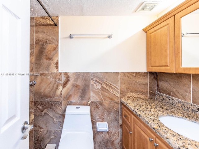 bathroom featuring vanity, a textured ceiling, a shower, tile walls, and toilet