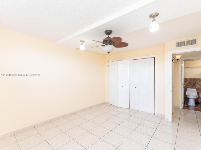 unfurnished bedroom with light tile patterned flooring, a closet, a textured ceiling, ceiling fan, and ensuite bath