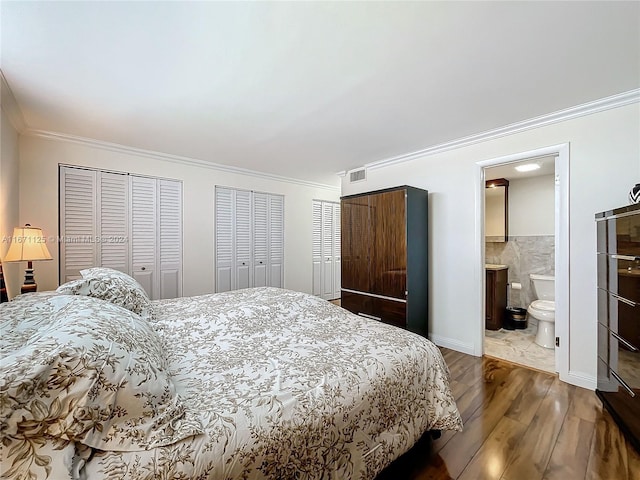 bedroom featuring wood finished floors, visible vents, ornamental molding, two closets, and ensuite bathroom