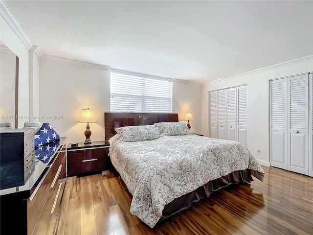 bedroom with wood finished floors, crown molding, and two closets