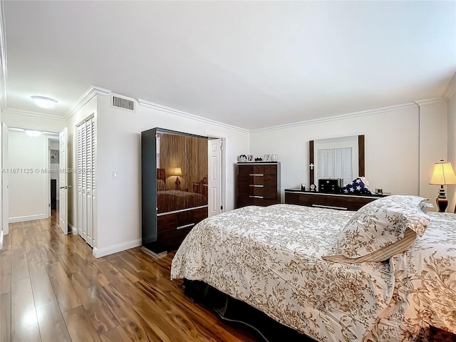 bedroom with wood finished floors, visible vents, baseboards, and ornamental molding