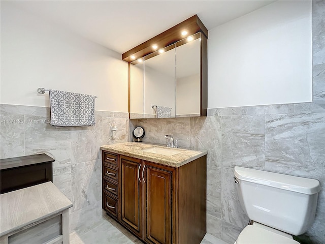 bathroom featuring wainscoting, toilet, vanity, and tile walls