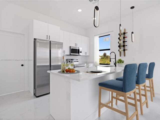 kitchen with white cabinets, sink, decorative light fixtures, appliances with stainless steel finishes, and a breakfast bar