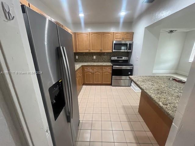 kitchen featuring decorative backsplash, light tile patterned floors, appliances with stainless steel finishes, and light stone countertops