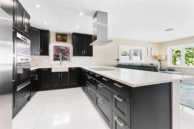 kitchen featuring island exhaust hood, kitchen peninsula, tasteful backsplash, sink, and light tile patterned floors