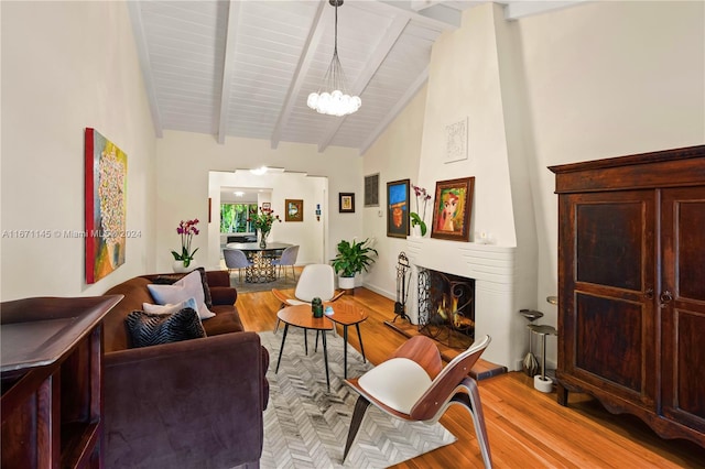 living room featuring an inviting chandelier, light hardwood / wood-style floors, a large fireplace, and beamed ceiling