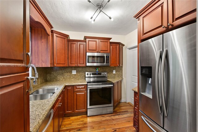 kitchen with appliances with stainless steel finishes, light stone counters, tasteful backsplash, light wood-type flooring, and sink