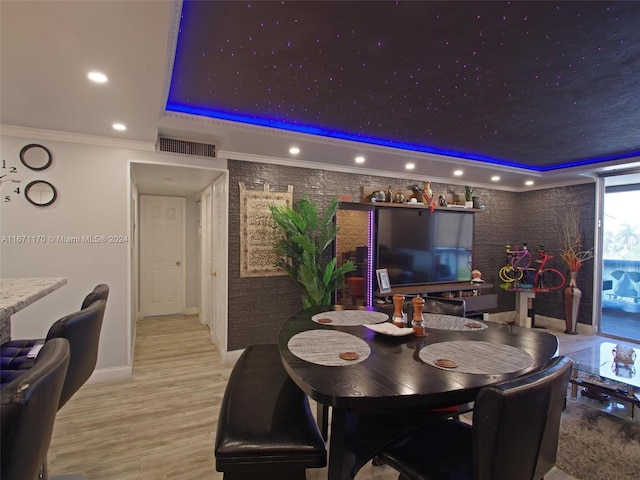 dining area with light wood-type flooring, a tray ceiling, and crown molding