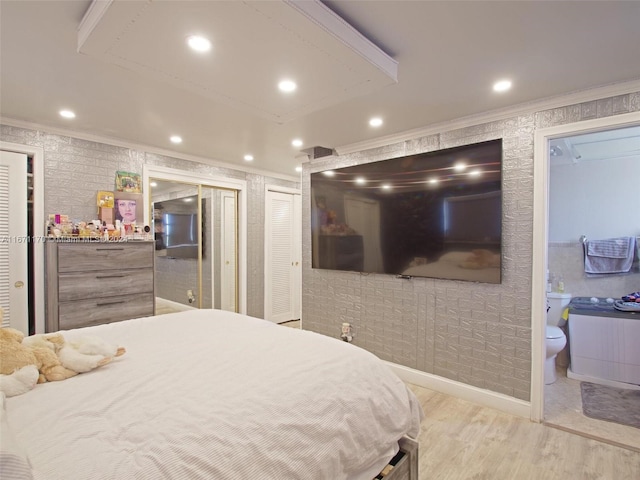 bedroom featuring light hardwood / wood-style floors, connected bathroom, ornamental molding, and multiple closets