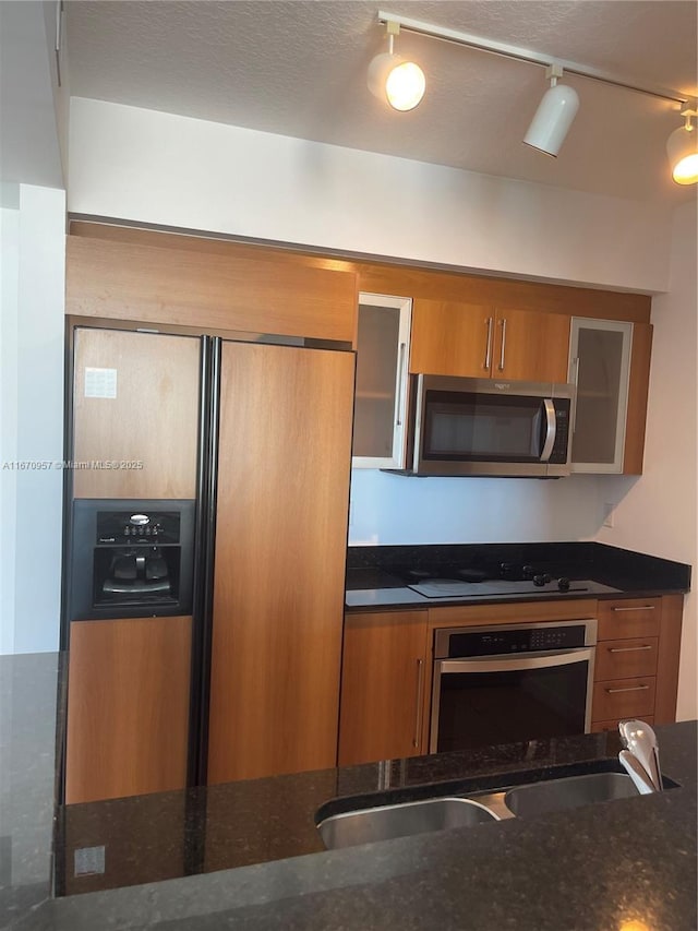 kitchen featuring sink, stainless steel appliances, track lighting, and dark stone countertops