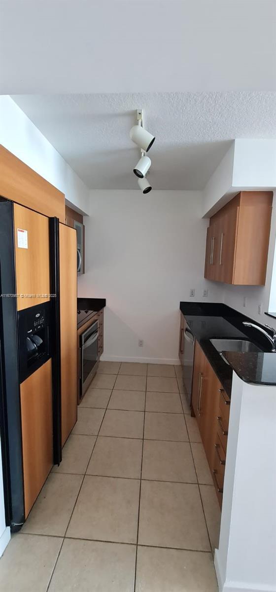 kitchen featuring light tile patterned flooring, black fridge with ice dispenser, a textured ceiling, and sink