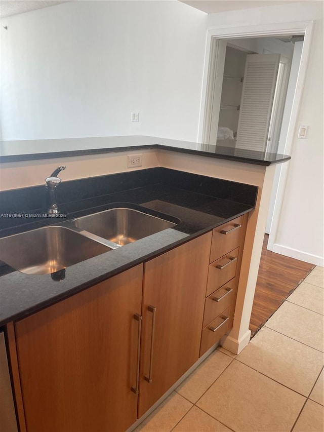 kitchen with dishwasher, light tile patterned floors, dark stone countertops, and sink