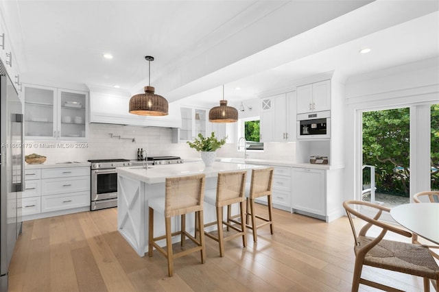 kitchen featuring an island with sink, white cabinetry, stainless steel appliances, light hardwood / wood-style floors, and decorative backsplash