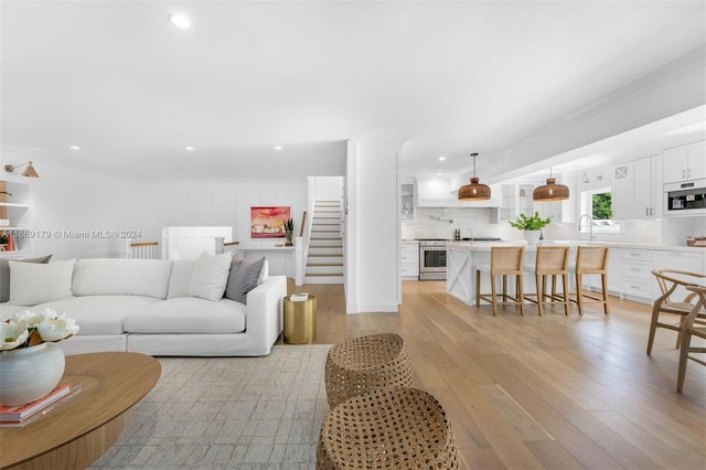 living room featuring light wood-type flooring, crown molding, and sink