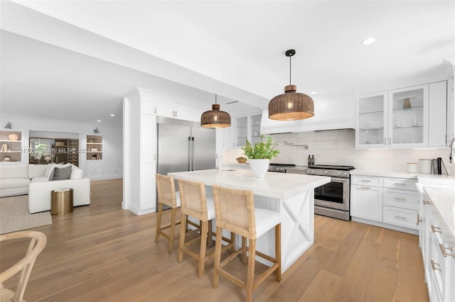 kitchen with decorative light fixtures, white cabinetry, appliances with stainless steel finishes, a kitchen breakfast bar, and light wood-type flooring