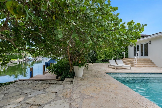 view of swimming pool featuring a patio, a boat dock, a water view, and french doors