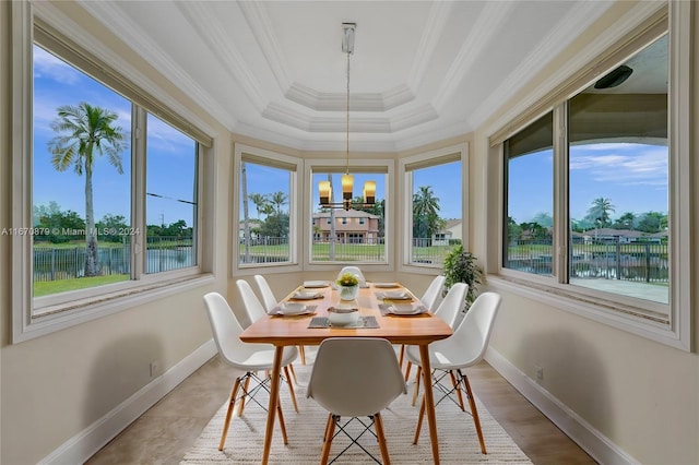 sunroom featuring a tray ceiling, a water view, an inviting chandelier, and a healthy amount of sunlight