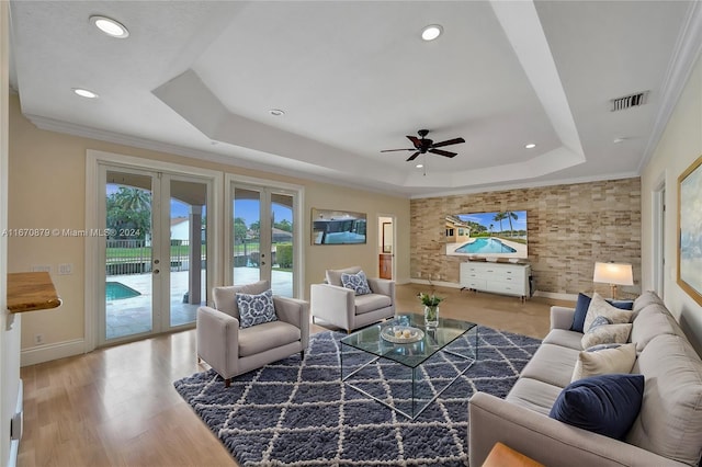 living room featuring french doors, hardwood / wood-style floors, ornamental molding, ceiling fan, and a tray ceiling