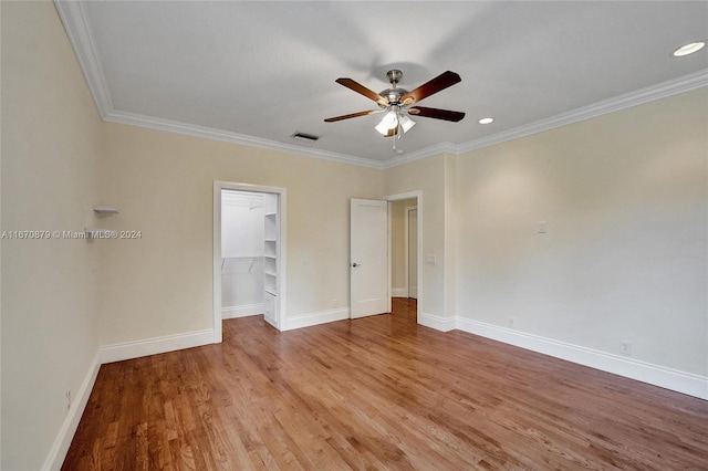 unfurnished bedroom with ceiling fan, a spacious closet, hardwood / wood-style floors, crown molding, and a closet