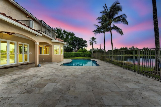 pool at dusk featuring ceiling fan, a patio, and a water view