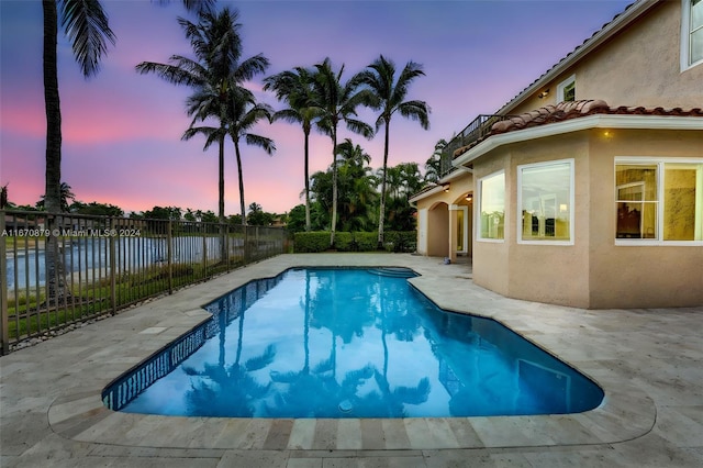 pool at dusk with a water view and a patio