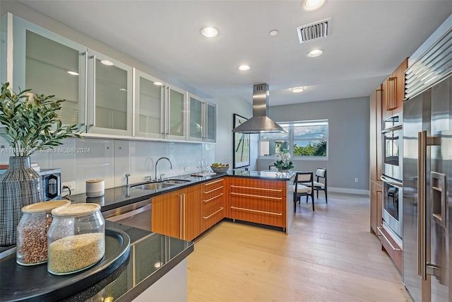 kitchen featuring appliances with stainless steel finishes, kitchen peninsula, island exhaust hood, light wood-type flooring, and sink