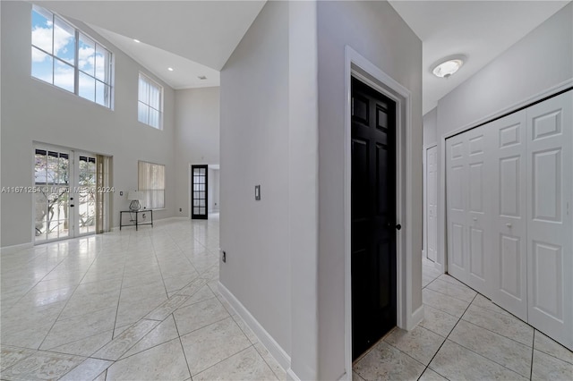 hall featuring french doors, light tile patterned floors, and a high ceiling