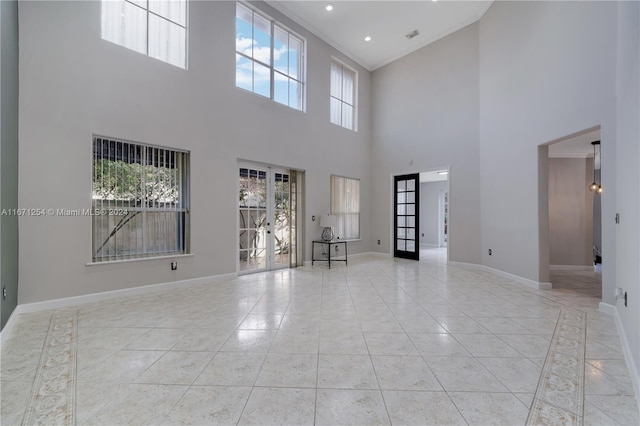 unfurnished living room featuring a healthy amount of sunlight, french doors, crown molding, and a towering ceiling