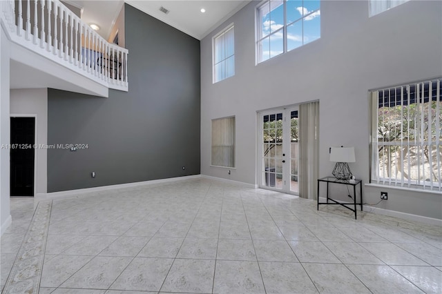 unfurnished living room with a towering ceiling, french doors, and light tile patterned floors