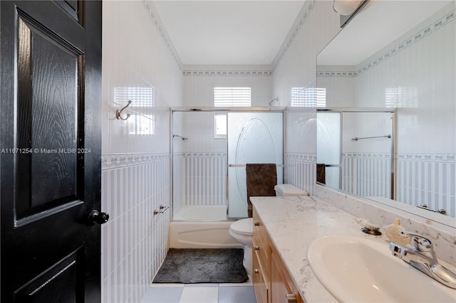 full bathroom featuring toilet, tile patterned flooring, vanity, tile walls, and combined bath / shower with glass door